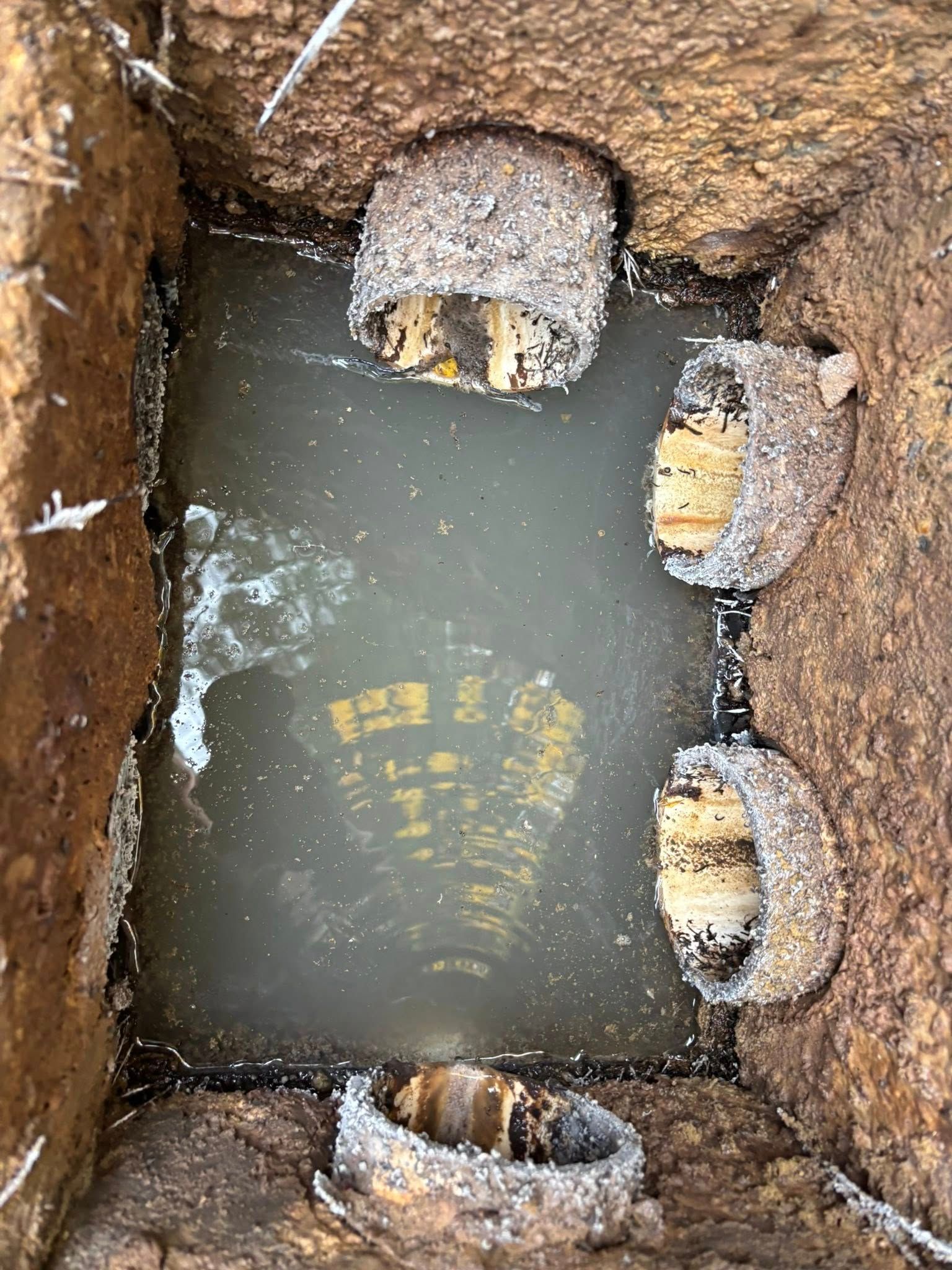 Four muddy boots or tires partly buried around a water-filled hole in dirt