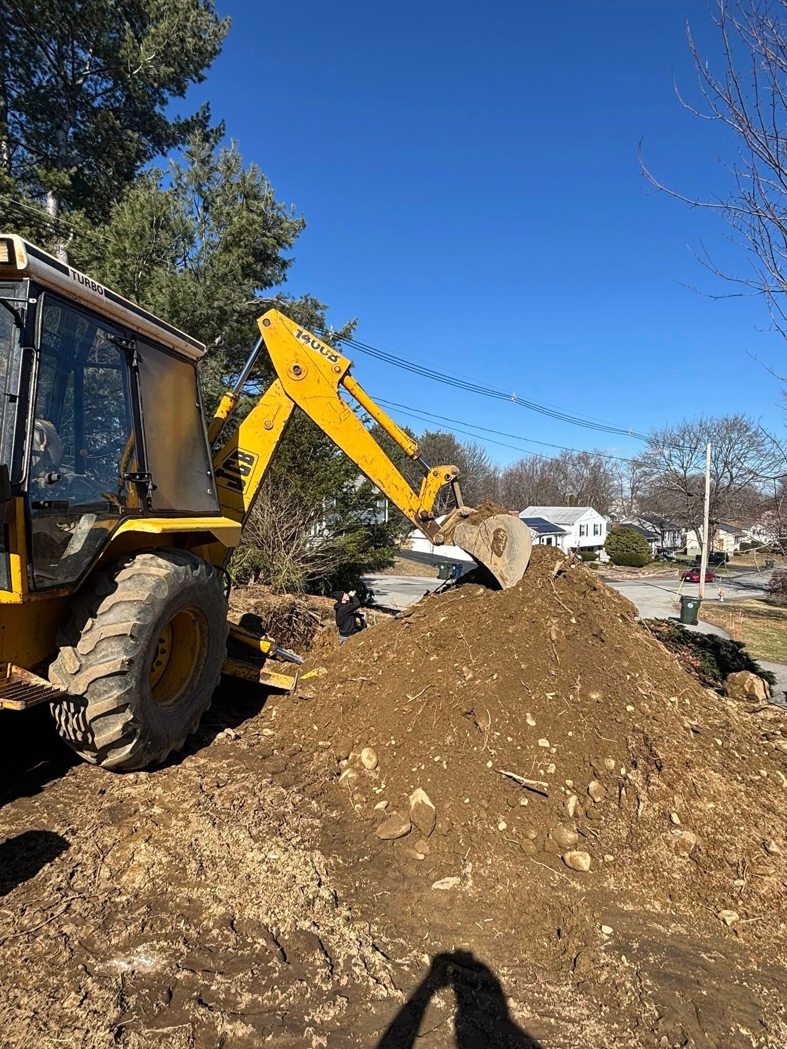 Backhoe loading a dirt pile at a sunny construction site