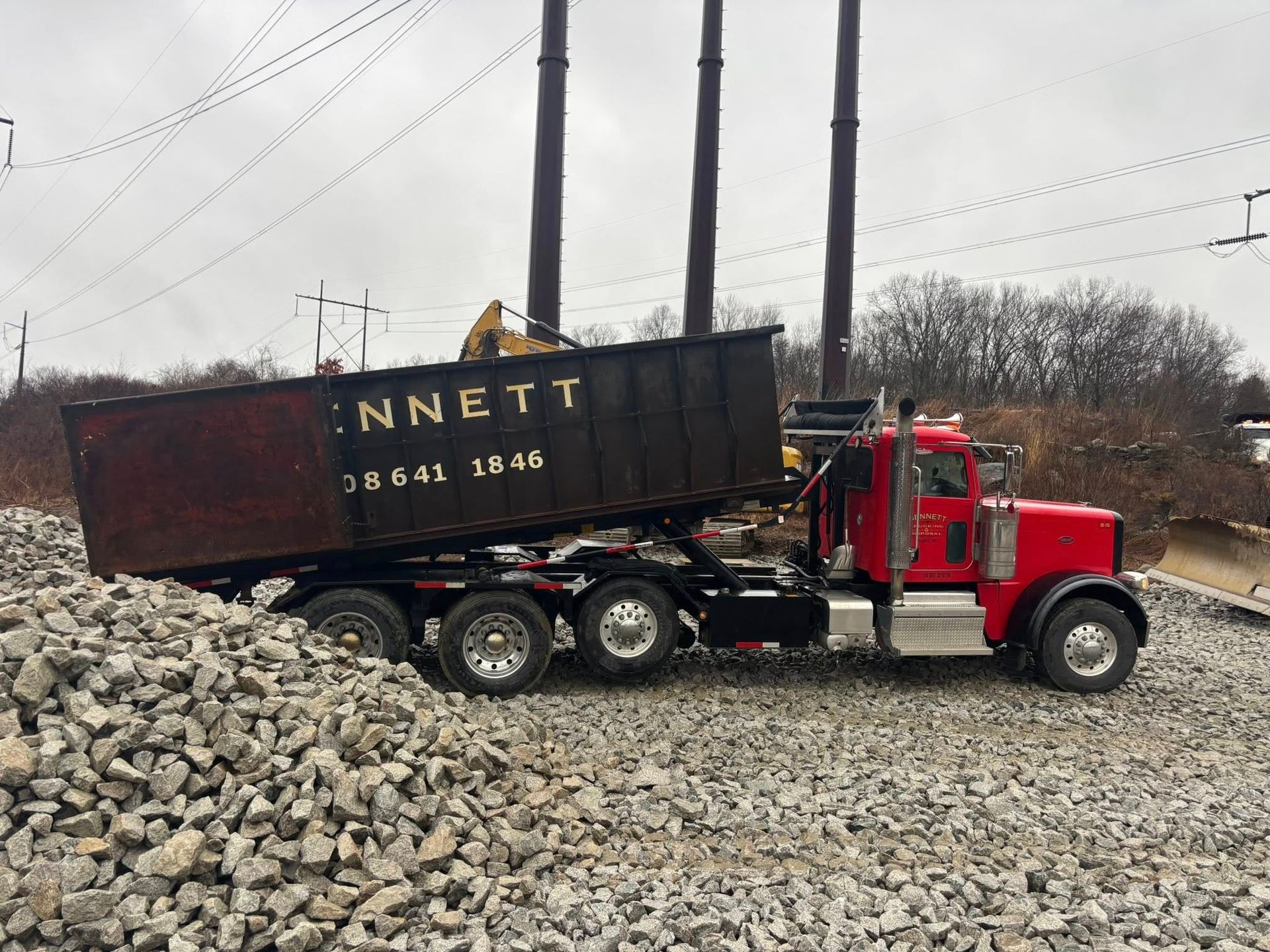 Red dump truck tipping a load of rocks at a gravel pile under power lines