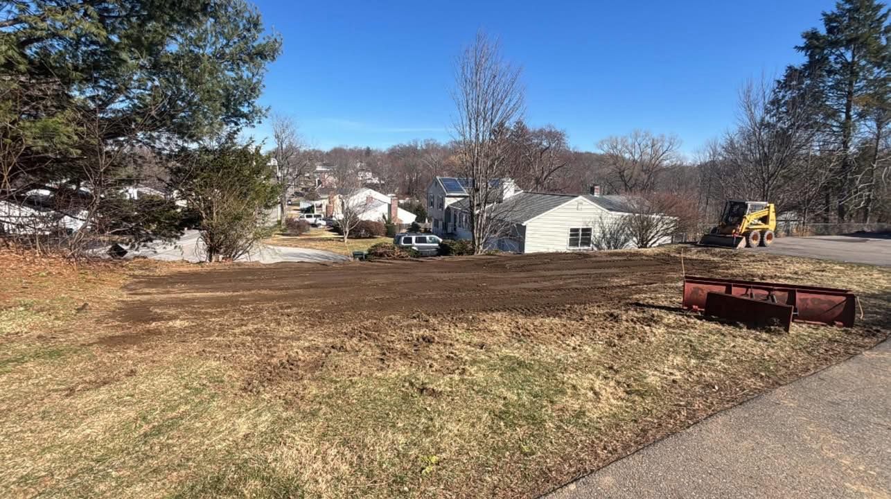 Open grassy lot with trees, houses, and construction equipment under a clear blue sky