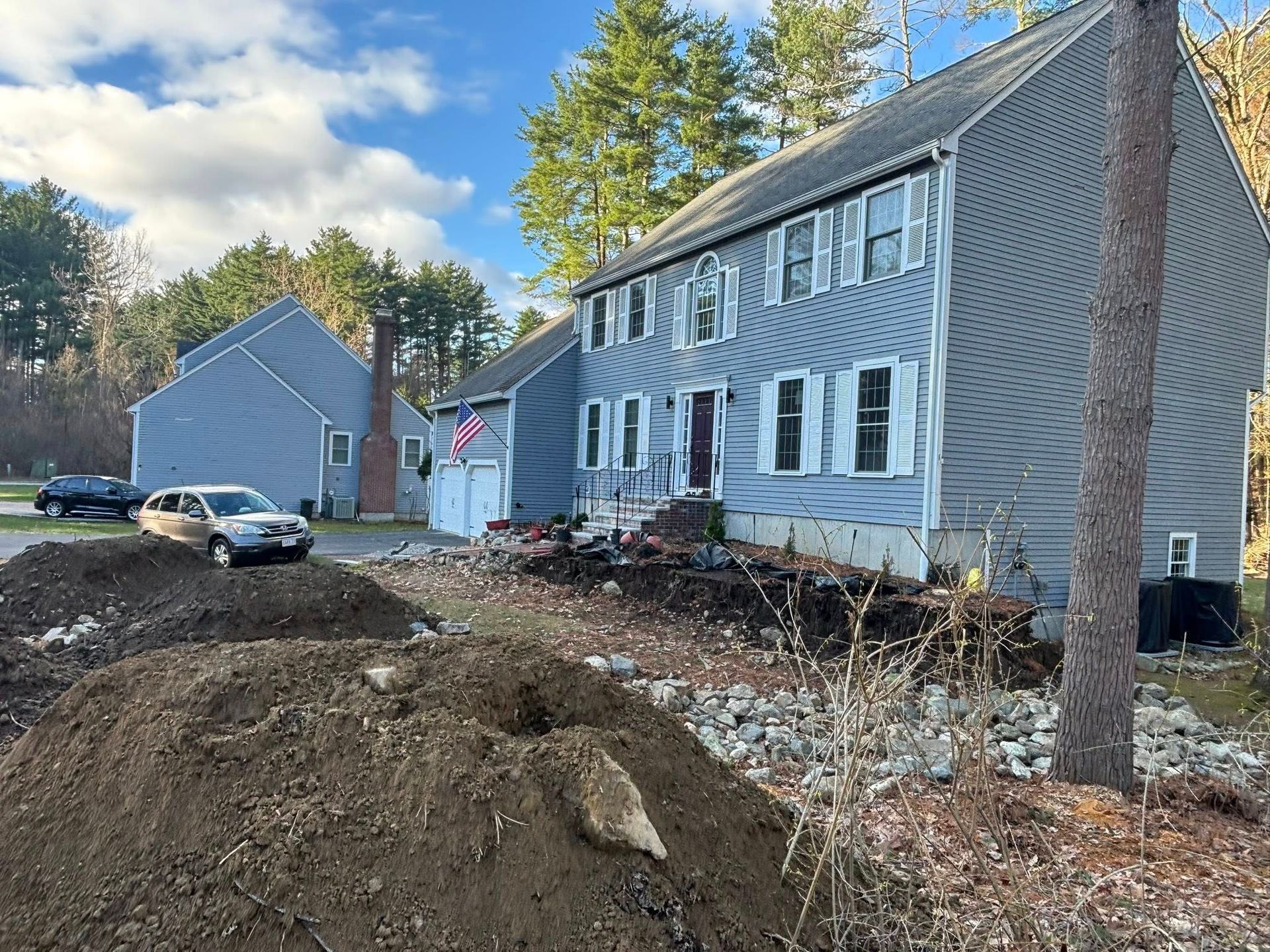 Row of blue townhouses beside a construction mound on a suburban street under a partly cloudy sky