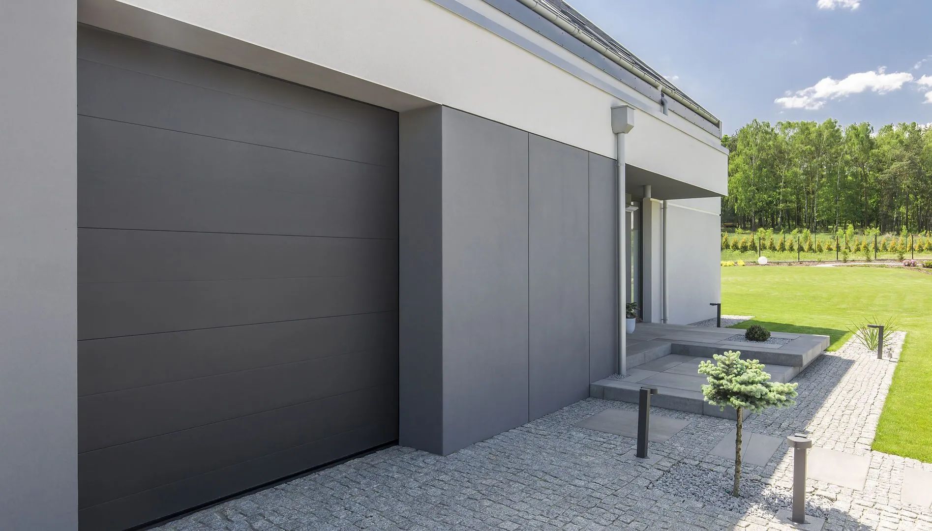 Gray garage door on a modern house with a concrete walkway and green lawn.