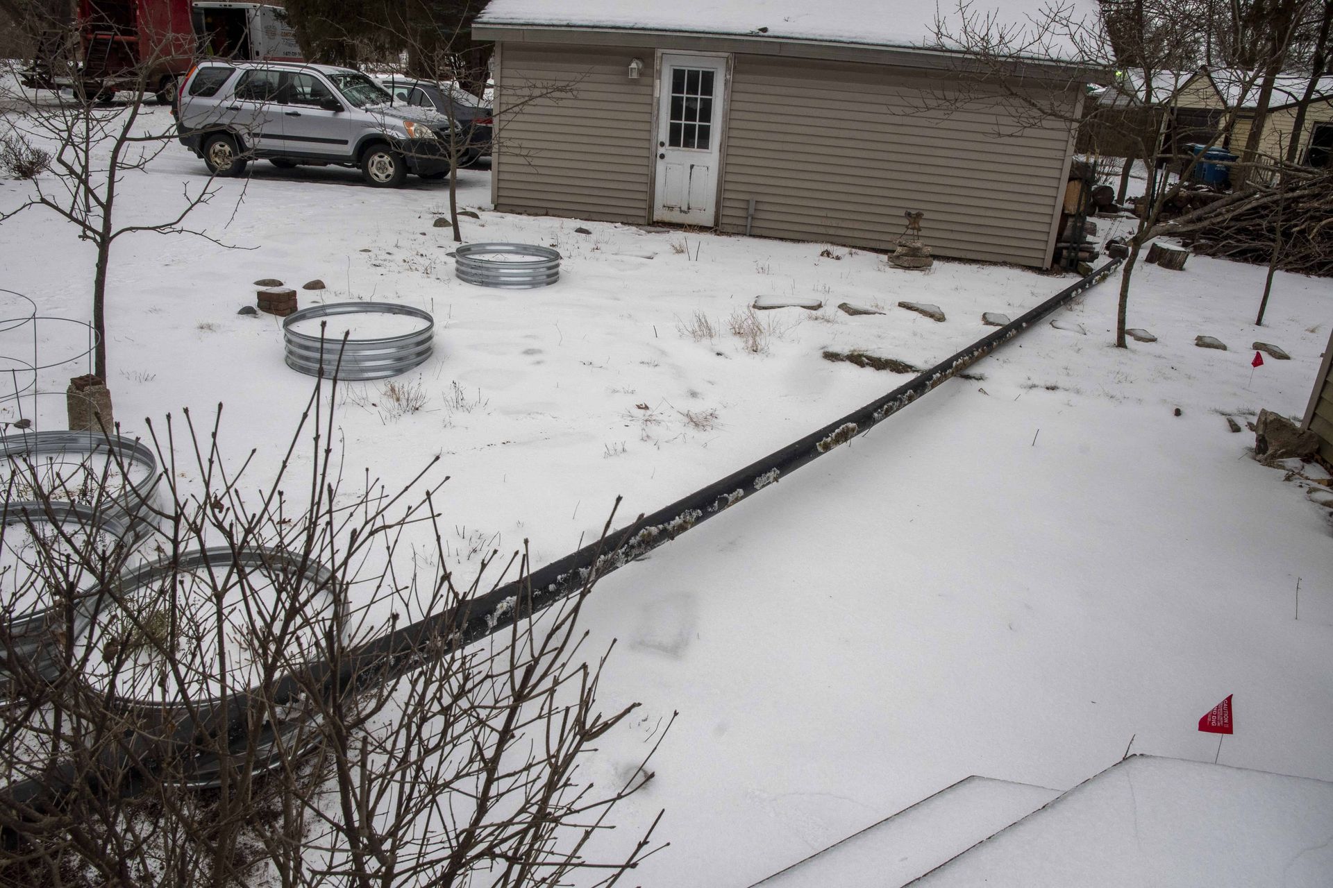 Snowy backyard with a shed, two metal rings, a car, and a long black object.