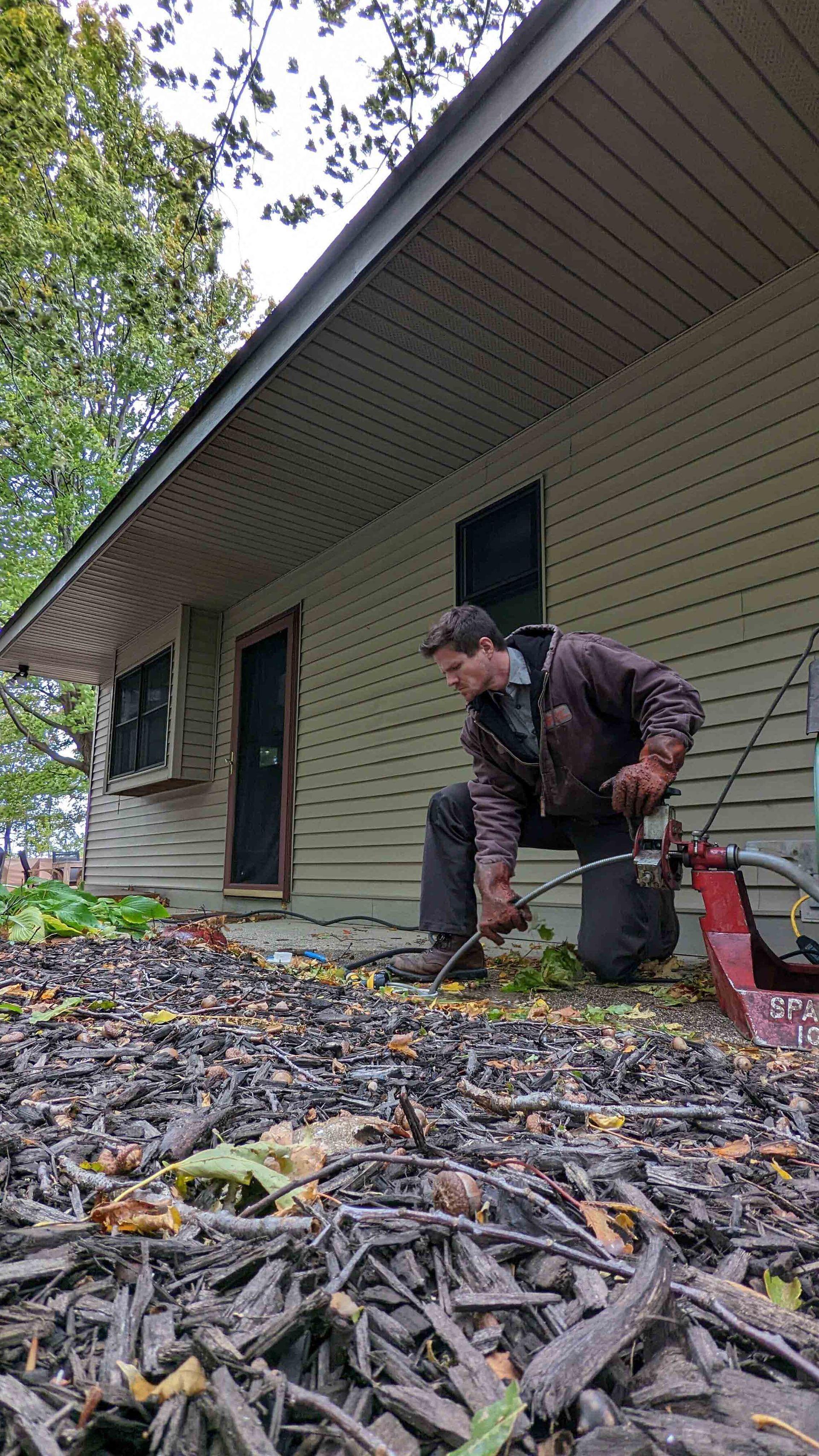 Man kneeling, working on ground near house, with mulch.