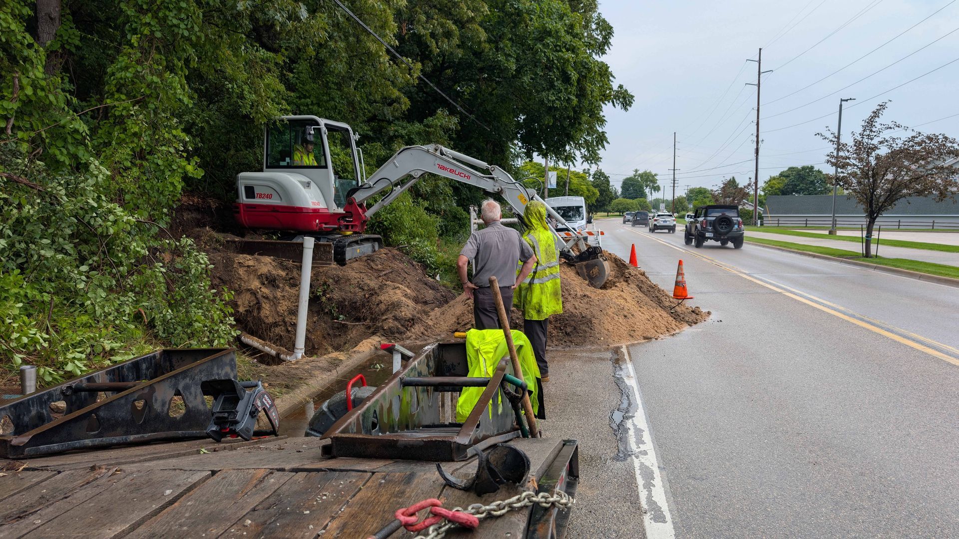 Construction site. Workers near a road with an excavator digging into a hillside, next to a pile of dirt.