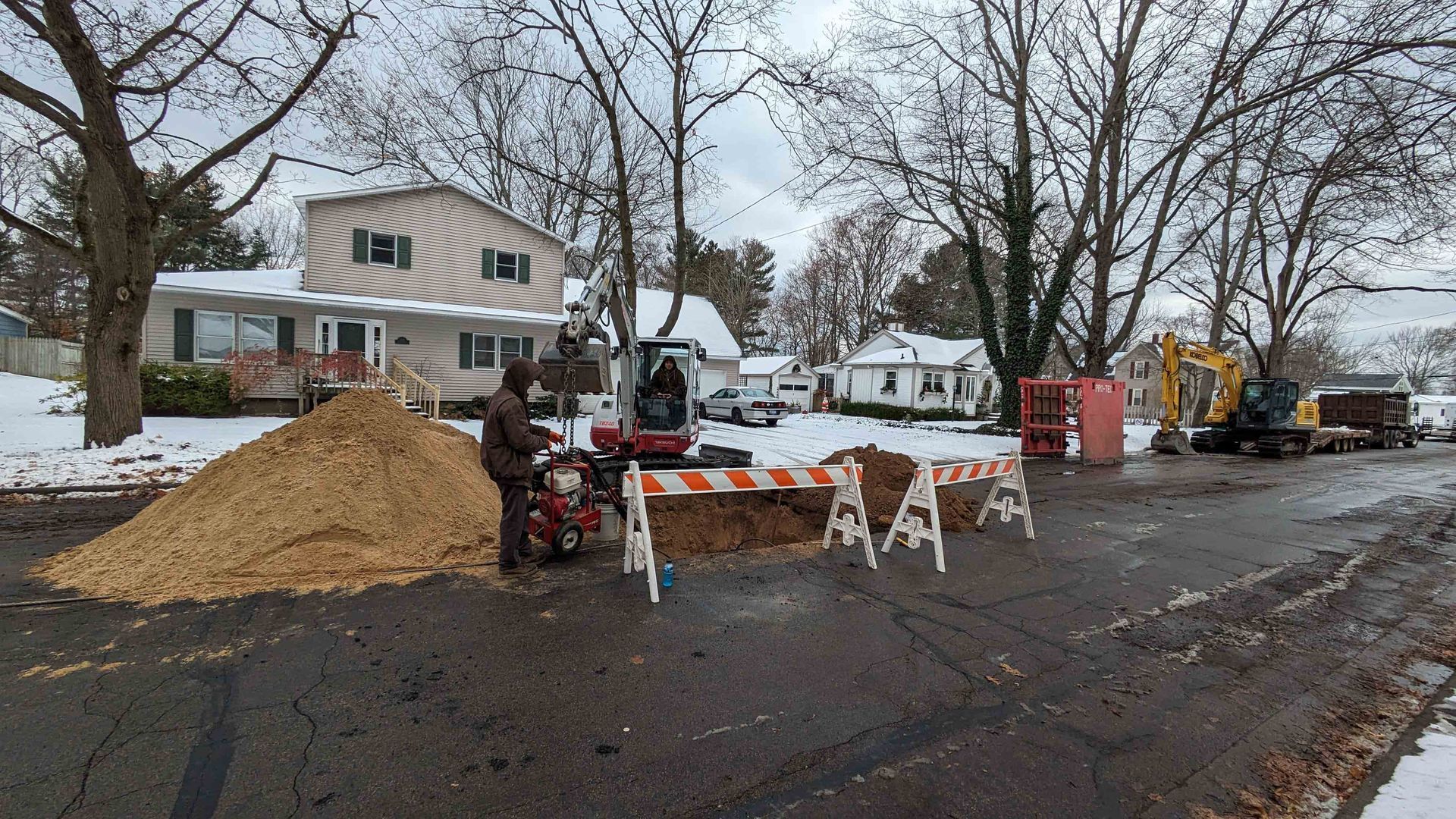 Construction site on a snow-covered street with a pile of wood chips and construction vehicles.