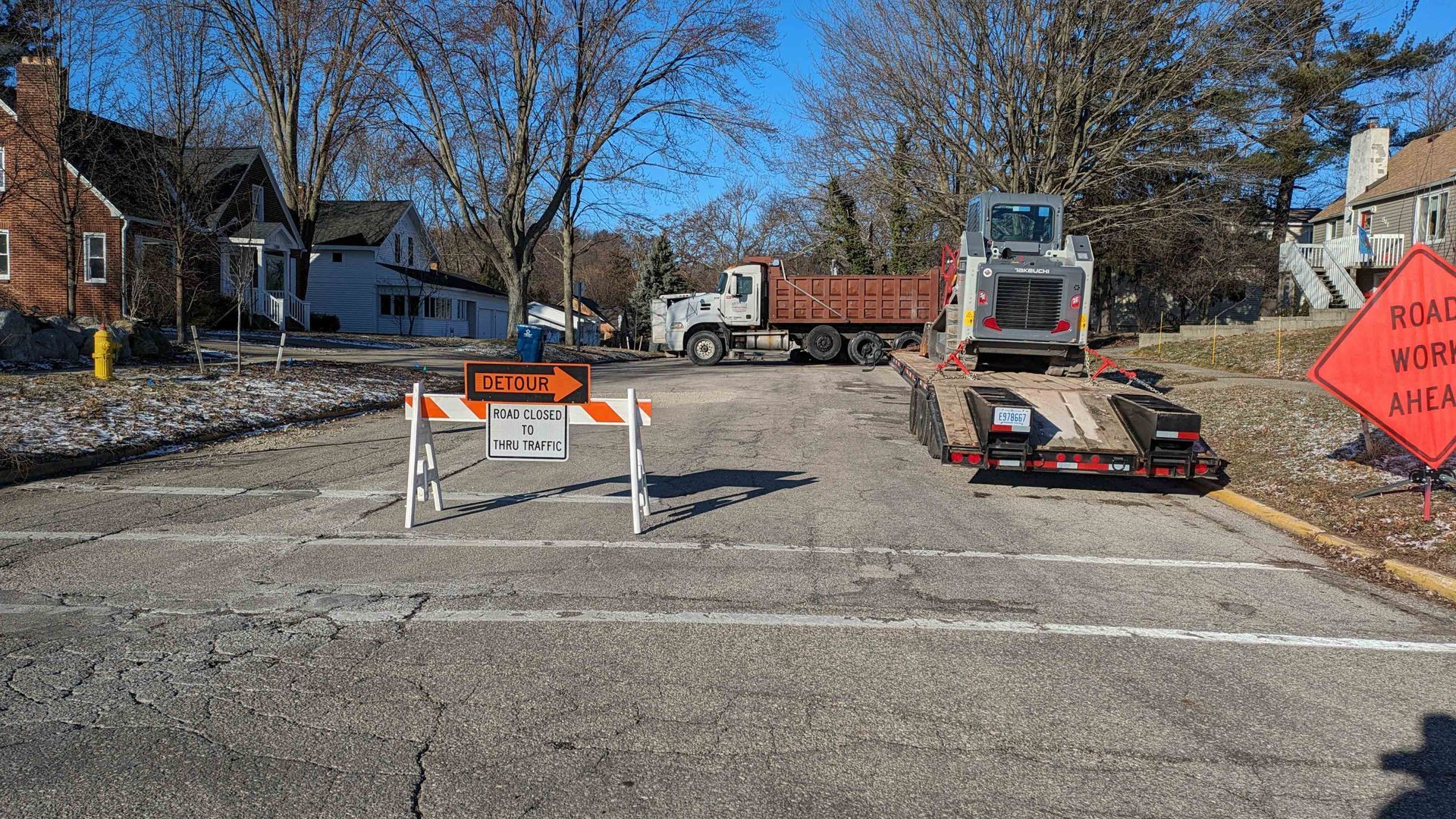 Road construction with truck, equipment, and detour signs on a street.