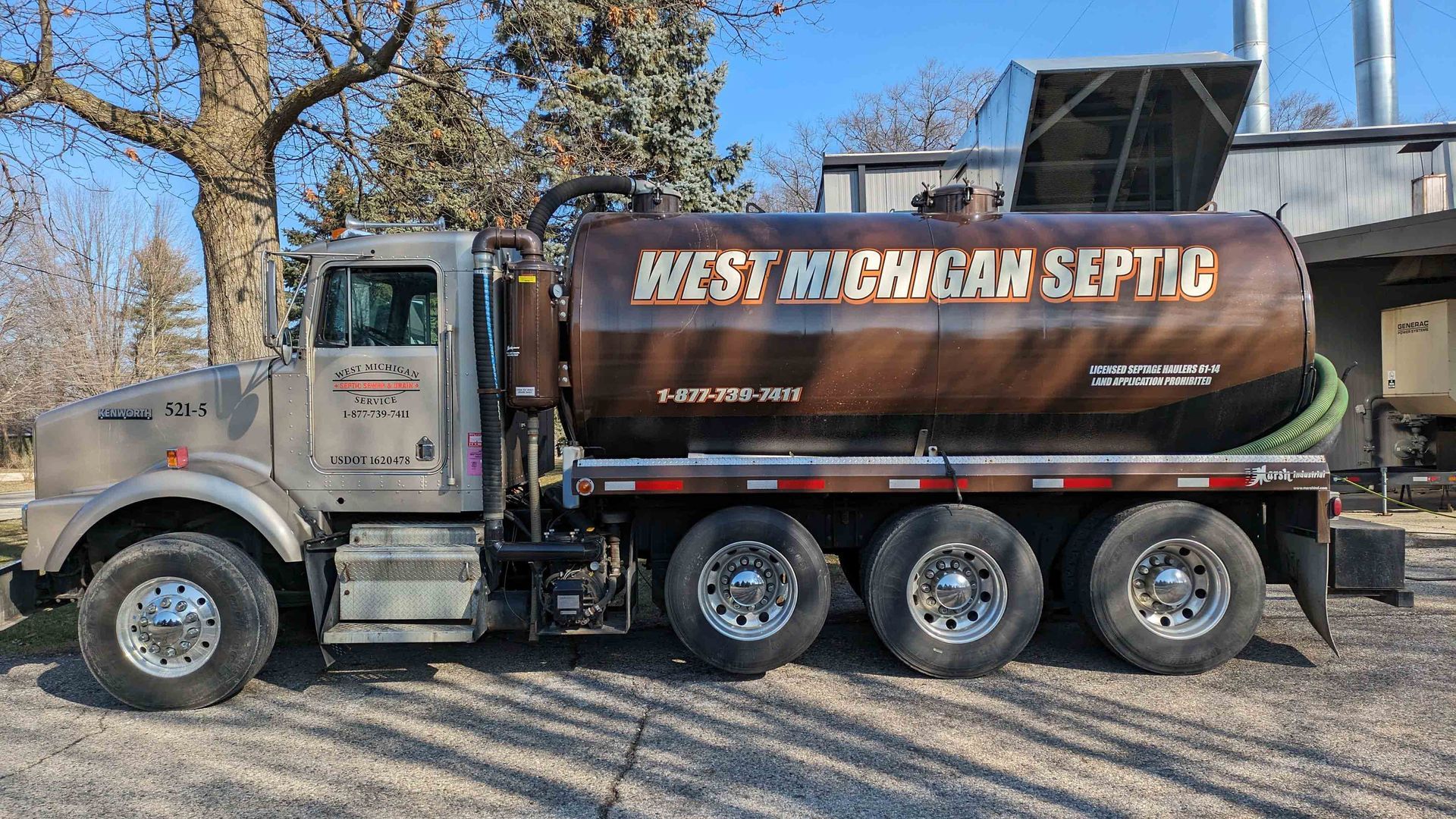 A septic tank truck with “West Michigan Septic” on its brown tank, parked on a gravel lot.