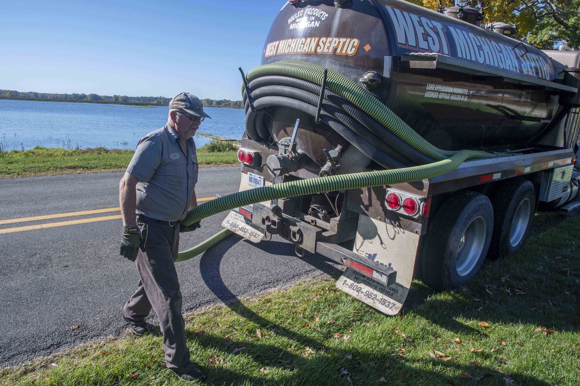 Man with septic truck and hose near a lake, preparing for service.