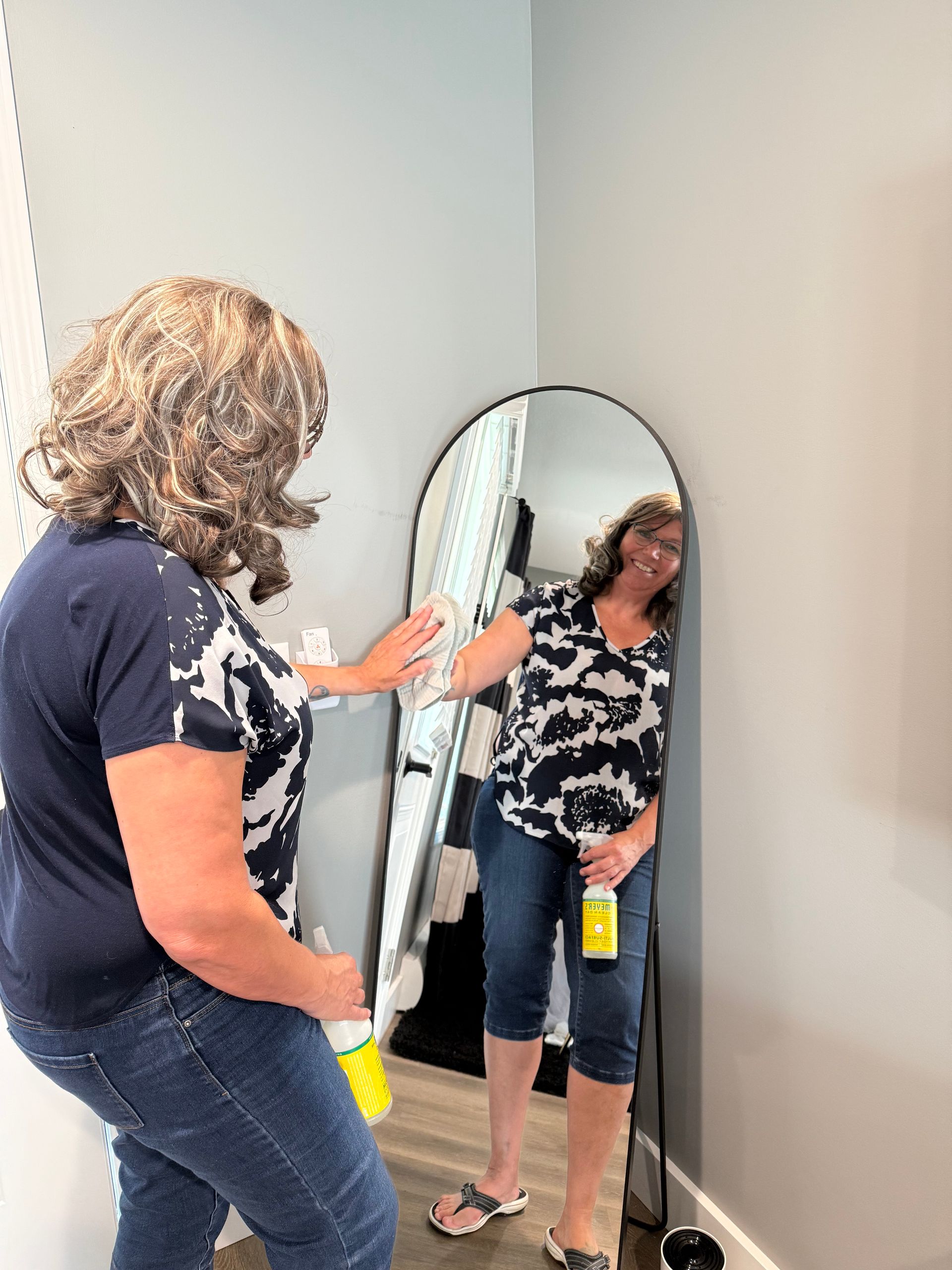 A woman is cleaning a mirror with a spray bottle.