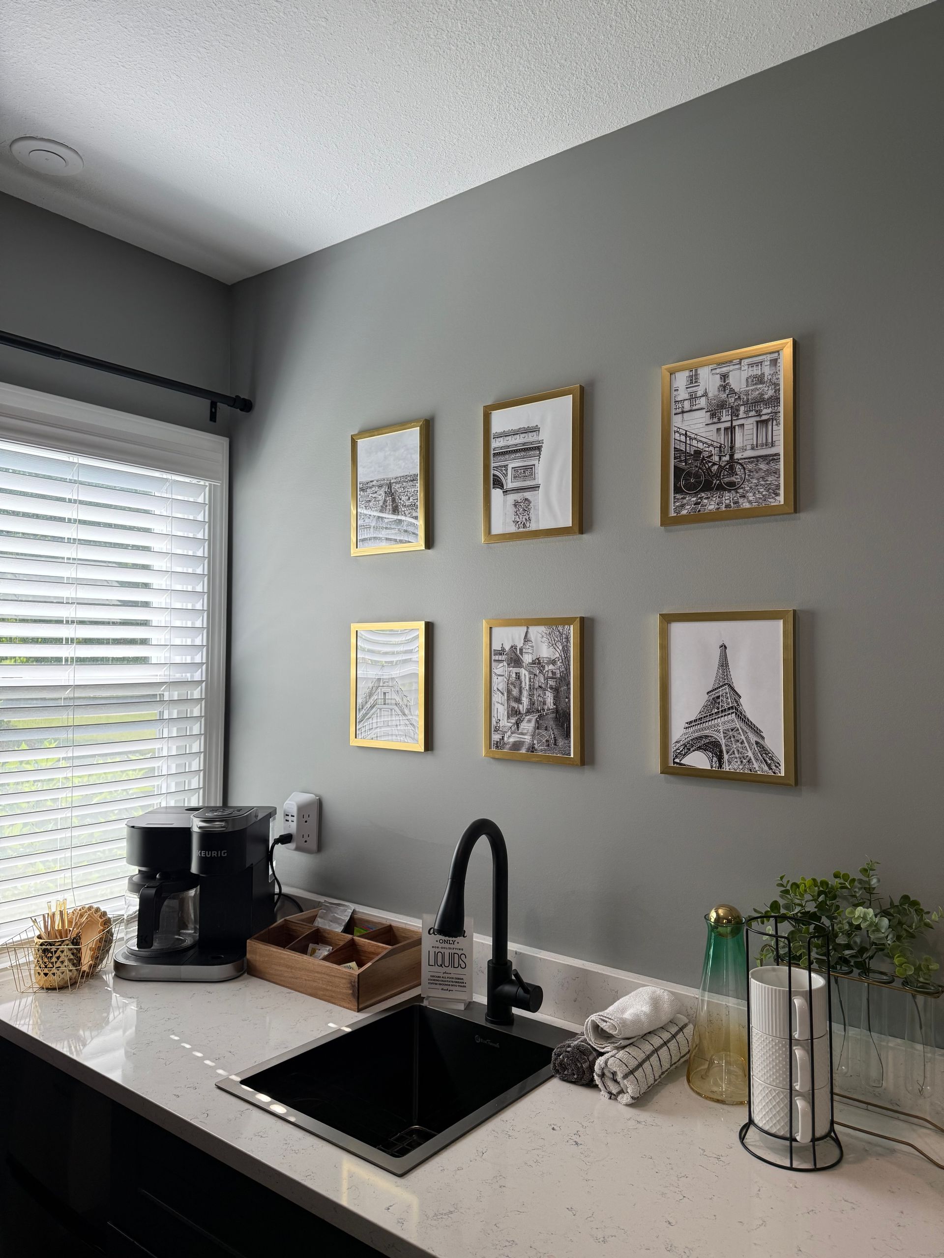 A kitchen with a sink , coffee maker , and pictures on the wall.