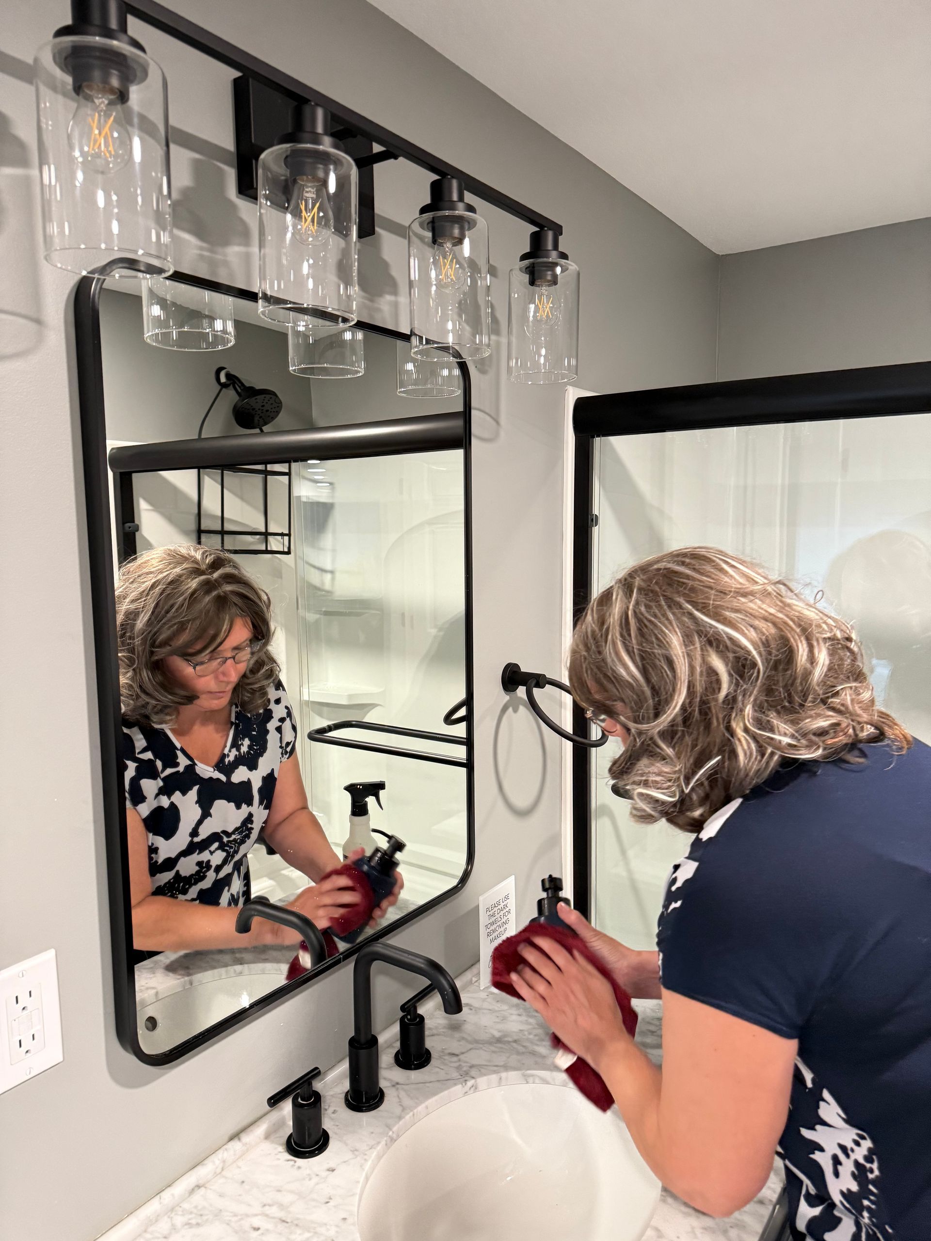 A woman is cleaning her face in front of a bathroom mirror.