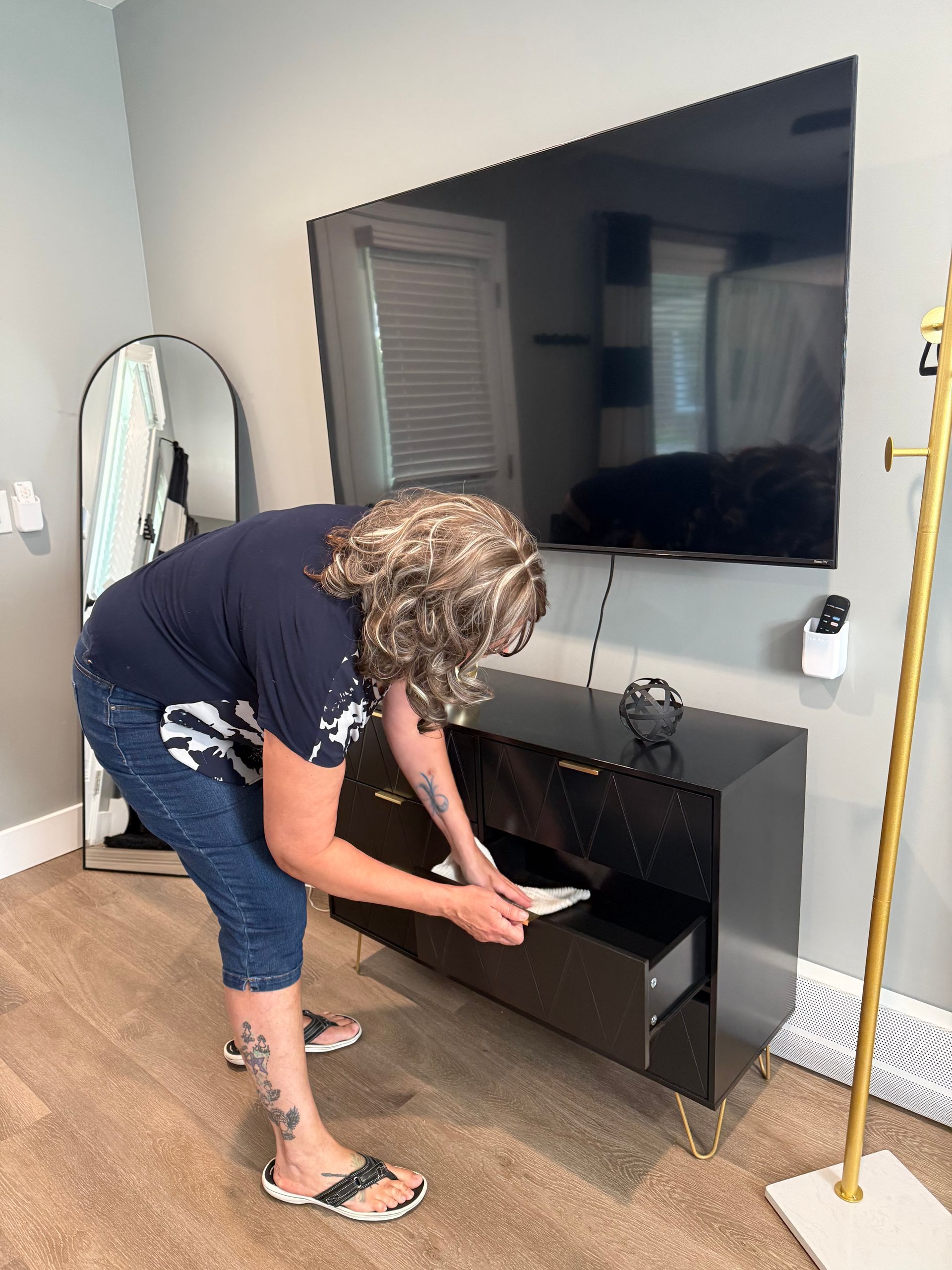 A woman is bending over to open a drawer in a living room.