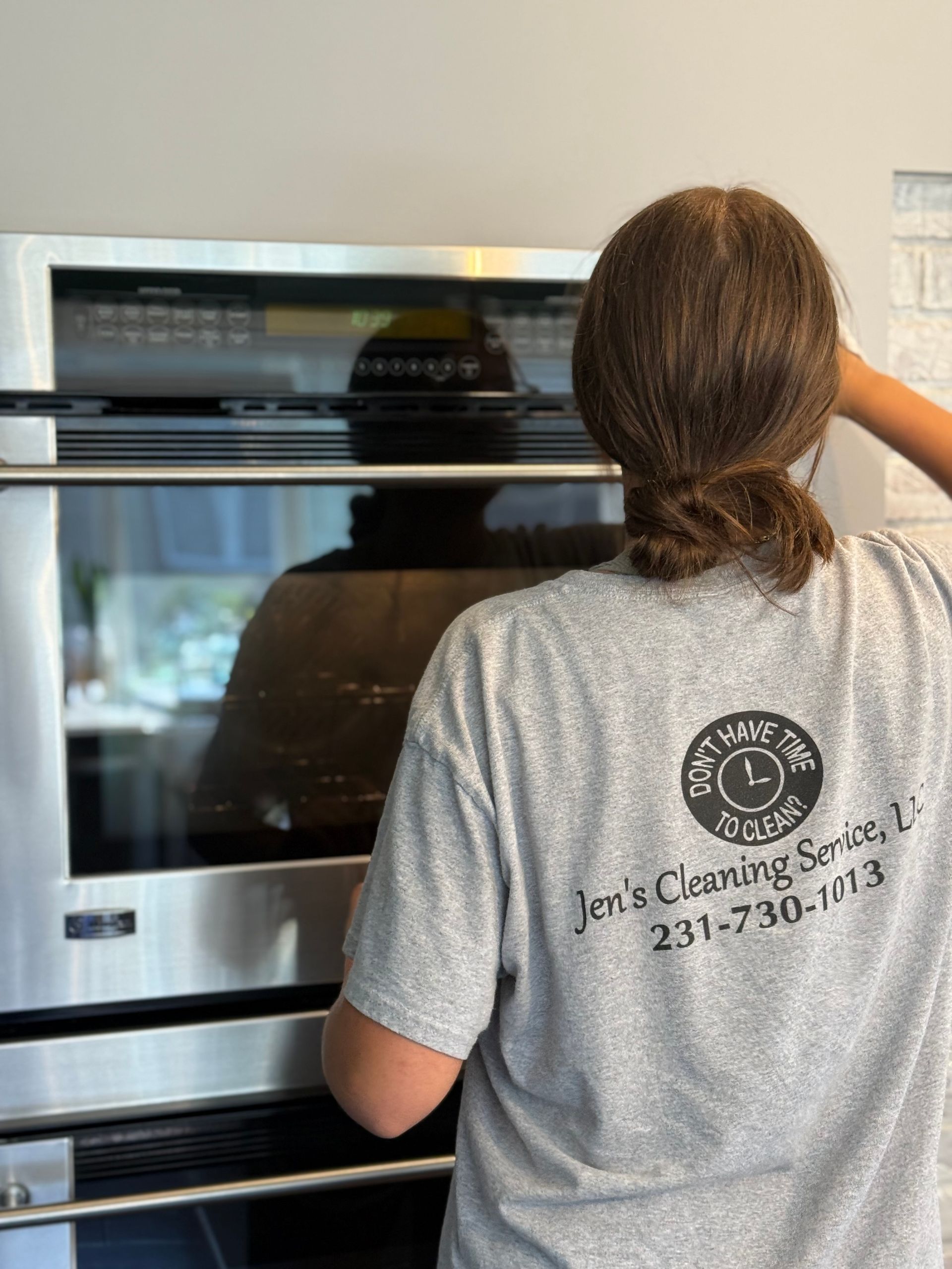 A woman is cleaning a stainless steel oven in a kitchen.