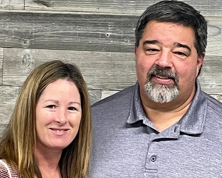 A man and a woman are posing for a picture in front of a wooden wall.