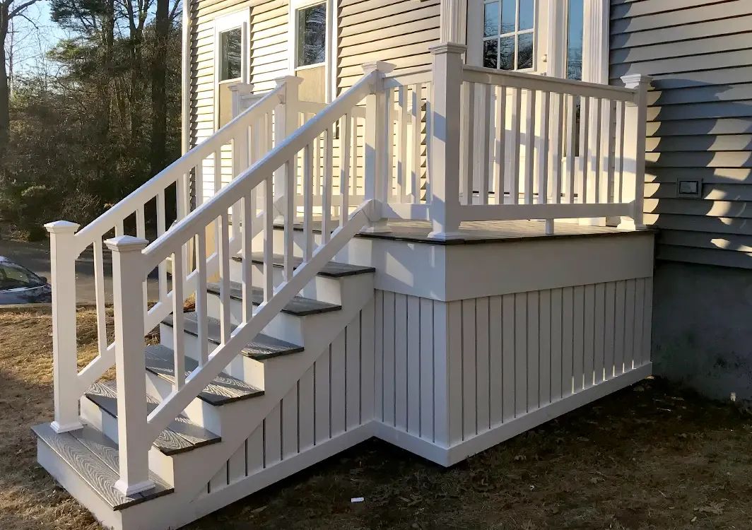 A white deck with stairs and a railing on the side of a house.