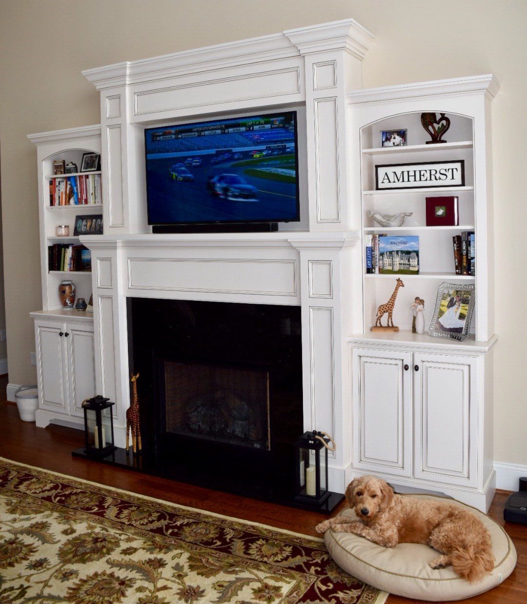A dog is laying on a pillow in front of a fireplace in a living room.