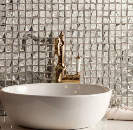 A bathroom sink with a gold faucet and a mosaic wall behind it.