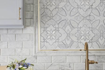 A kitchen with a sink and a floral tile wall.