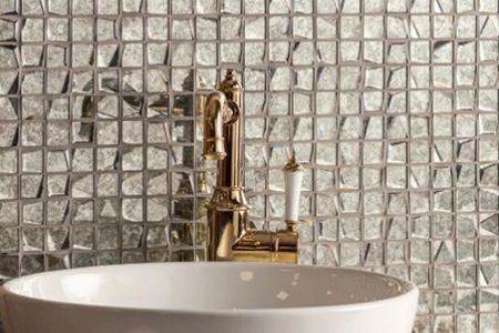 A bathroom sink with a gold faucet and mosaic tiles on the wall.