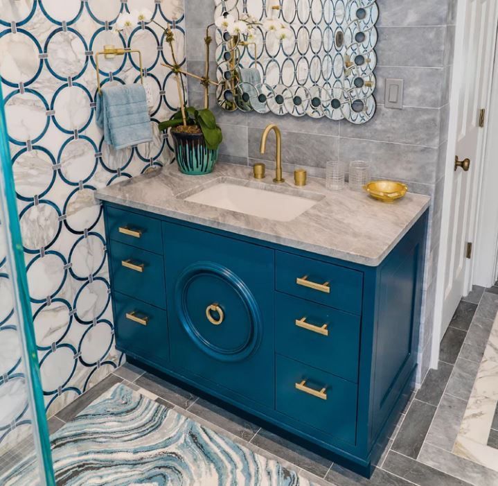 A bathroom with blue cabinets , a sink , a mirror and a rug.