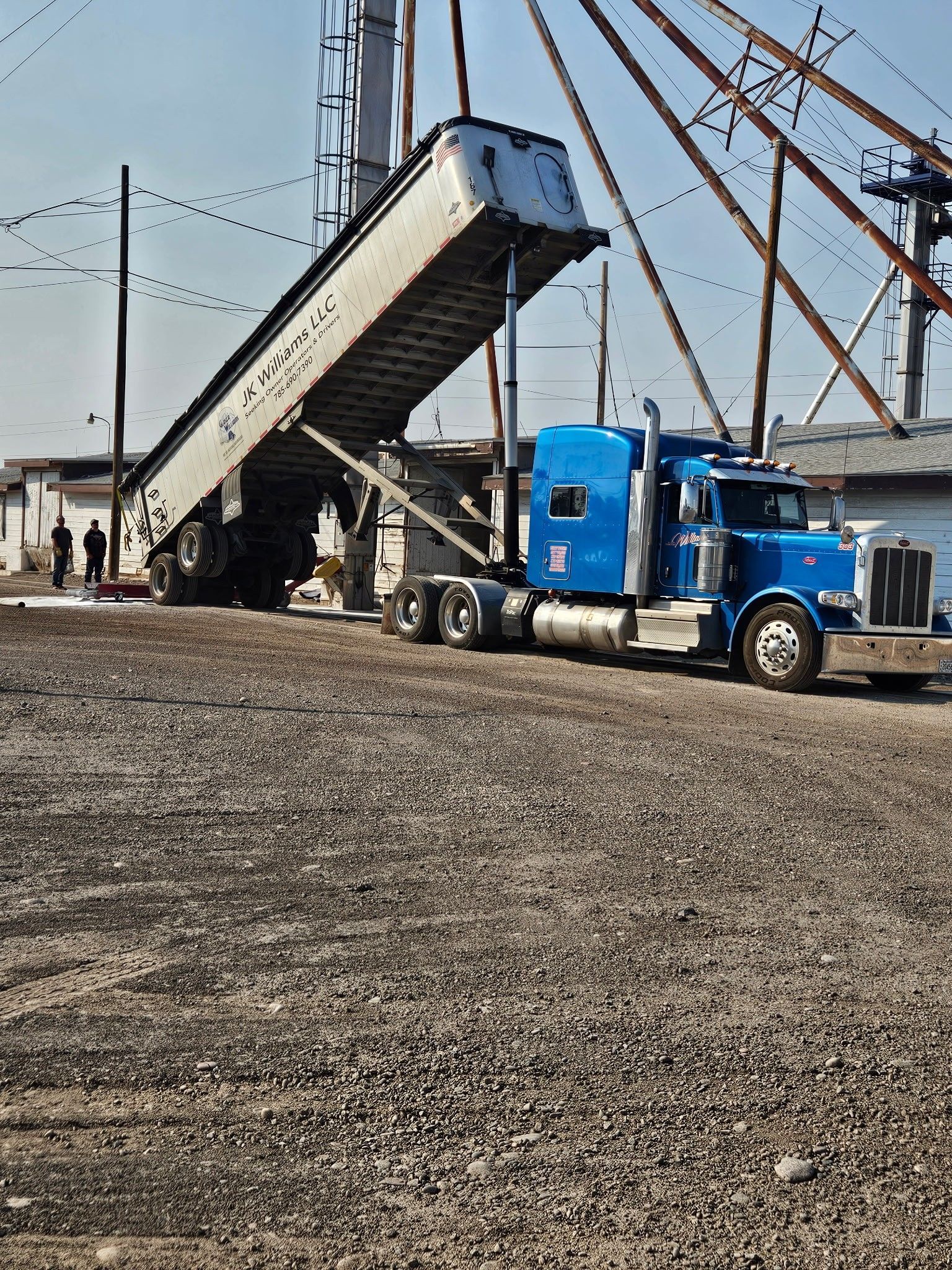 Blue semi-truck dumping a load at a gravel yard beside industrial structures