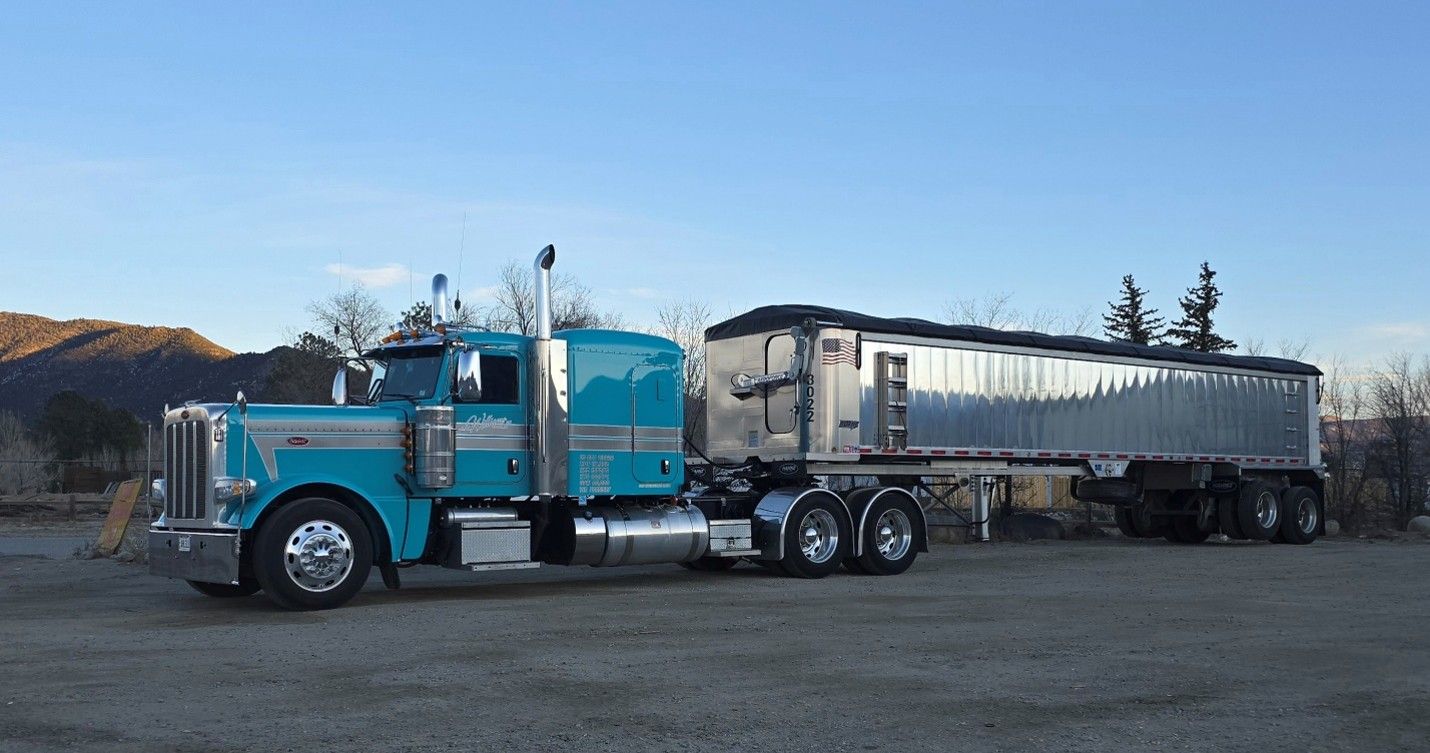 Blue semi truck hauling a silver trailer parked on gravel under a clear sky