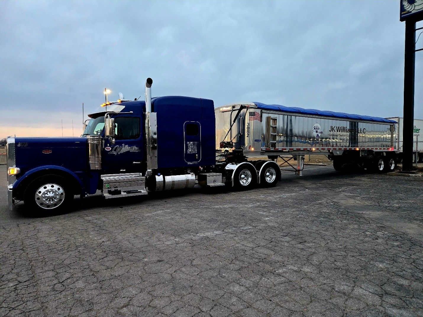 Blue semi truck hauling a silver trailer parked on gravel at dusk