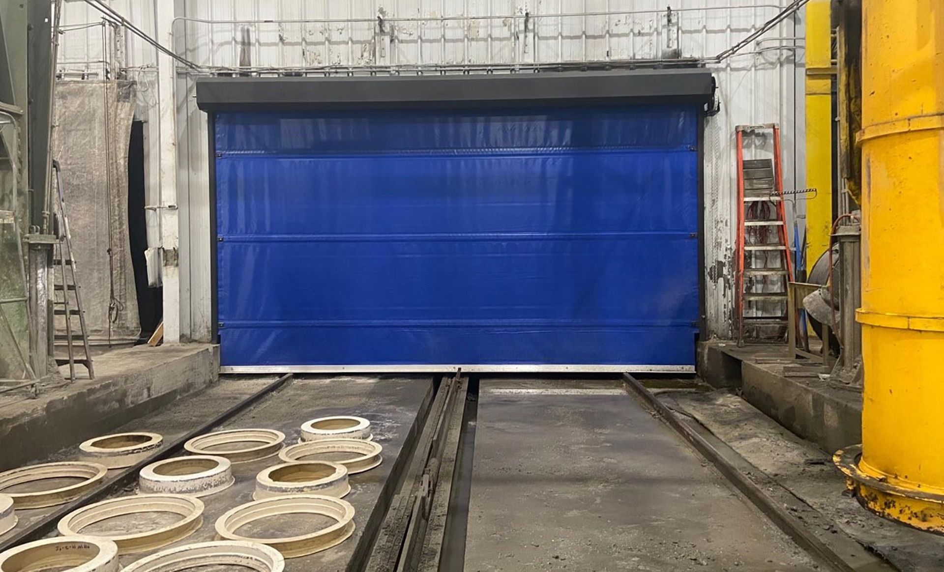 A blue door is sitting on top of a train track in a factory.