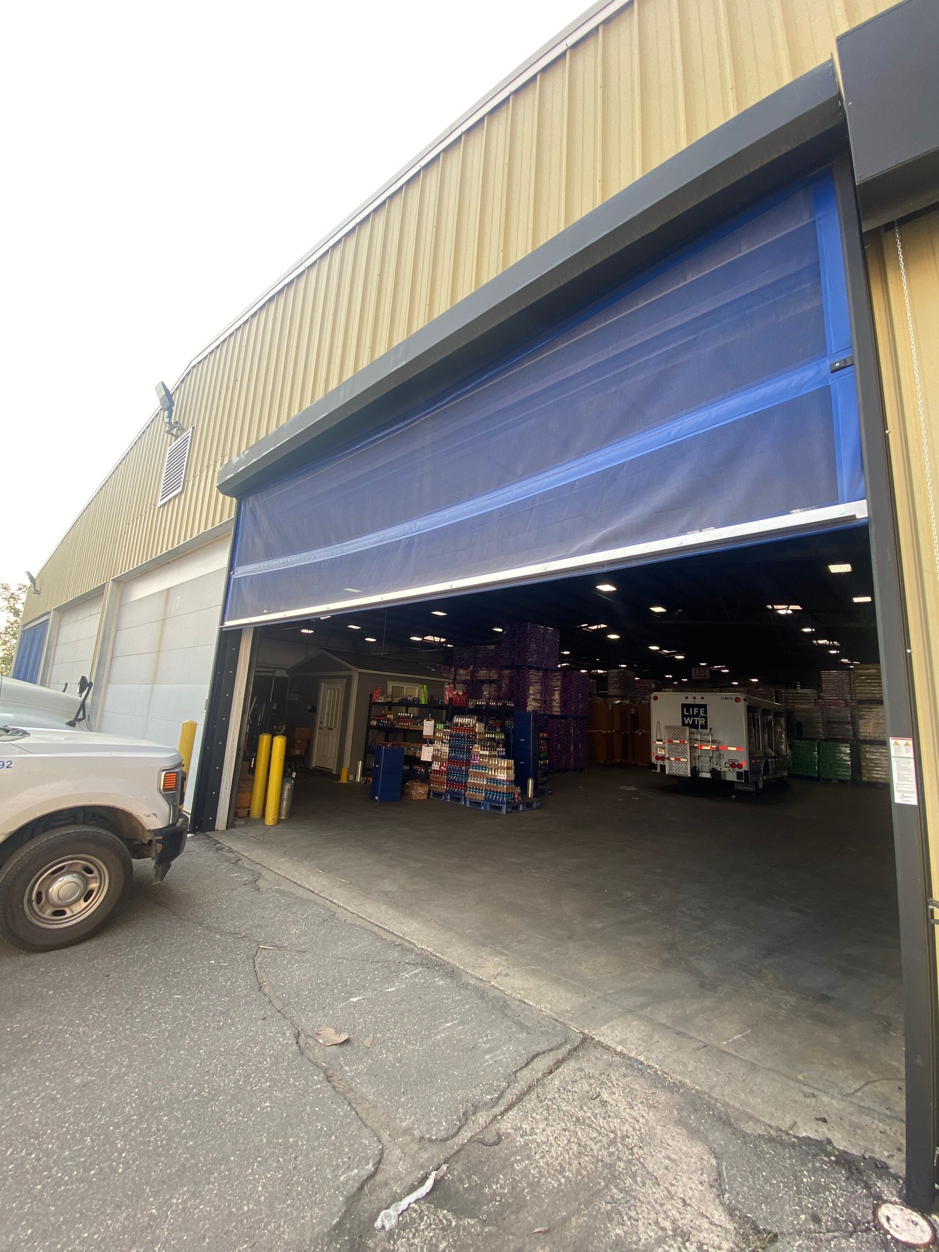 A truck is parked in front of a large warehouse with a blue door.
