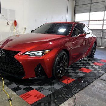 A red car is parked on a checkered floor in a garage