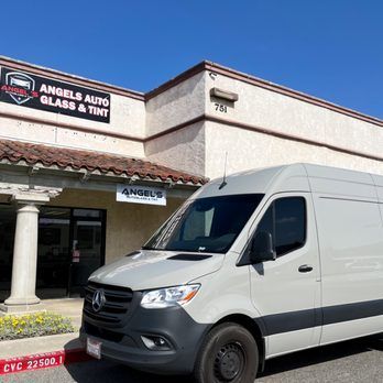 A white van is parked in front of an auto glass and tint shop