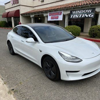 A white Tesla model 3 is parked in front of a window tinting shop