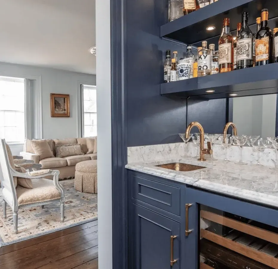 Built-in navy bar with gold fixtures, marble counter, and wine fridge. Living room with couch is visible in background.