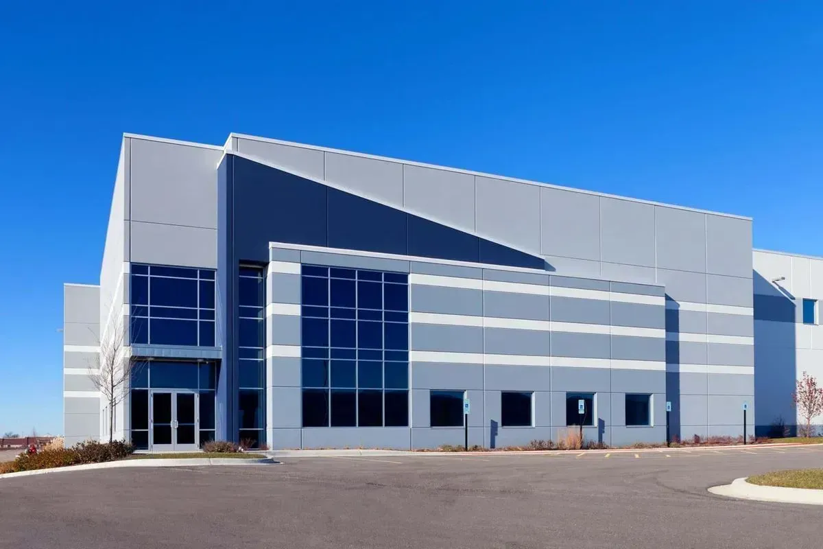 Modern gray industrial building with large windows and blue sky.