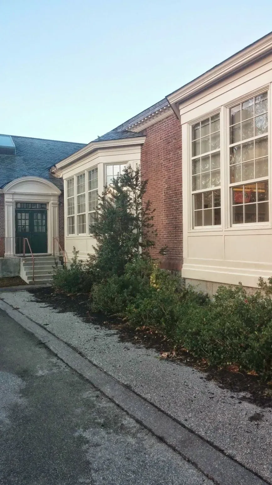 Brick building with large windows and a green door, surrounded by landscaping.