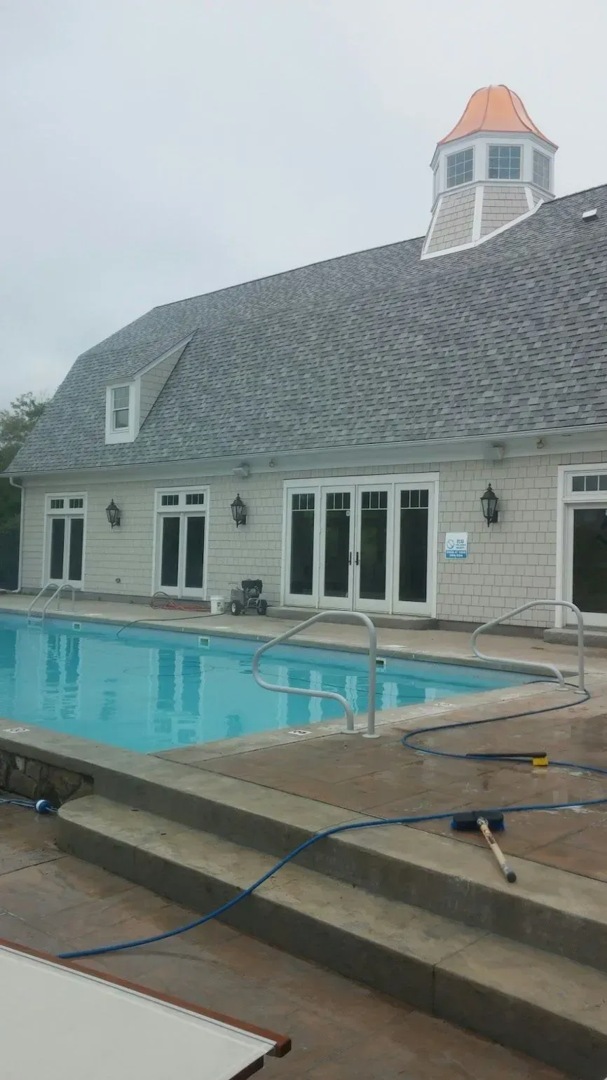 Swimming pool with a light-colored building, featuring large windows and a gray roof, under an overcast sky.