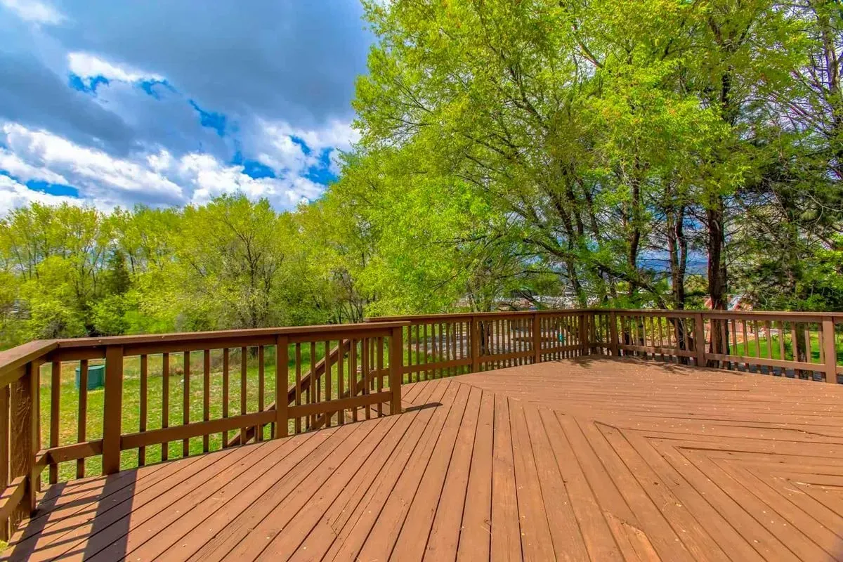 Wooden deck with brown railings overlooking a green landscape and blue sky with clouds.