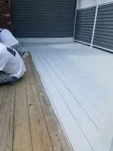 Deck being painted white; partially painted with bags nearby, dark siding.