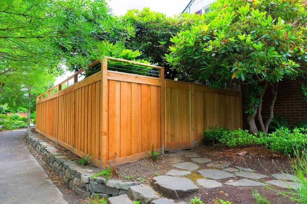 Wooden fence bordering a lush garden path with trees and greenery.