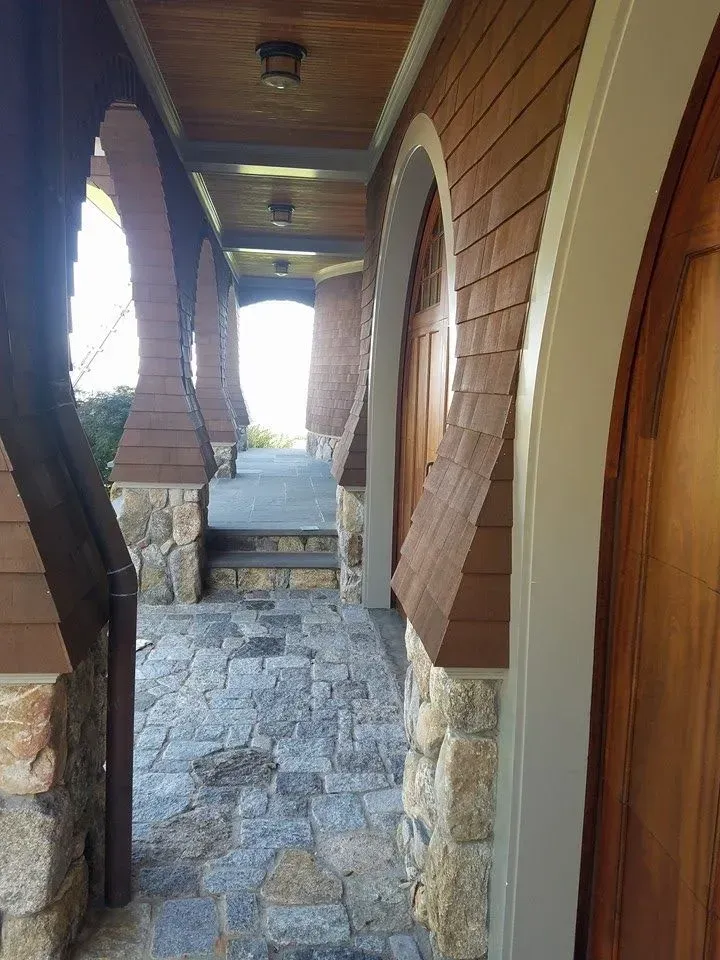 Stone and brick walkway with arched entryways, brown cedar siding, and stone columns.