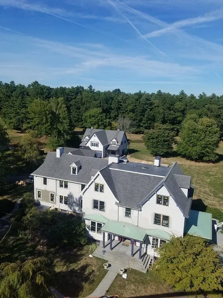 Aerial view of white buildings with gray roofs, surrounded by trees on a sunny day.