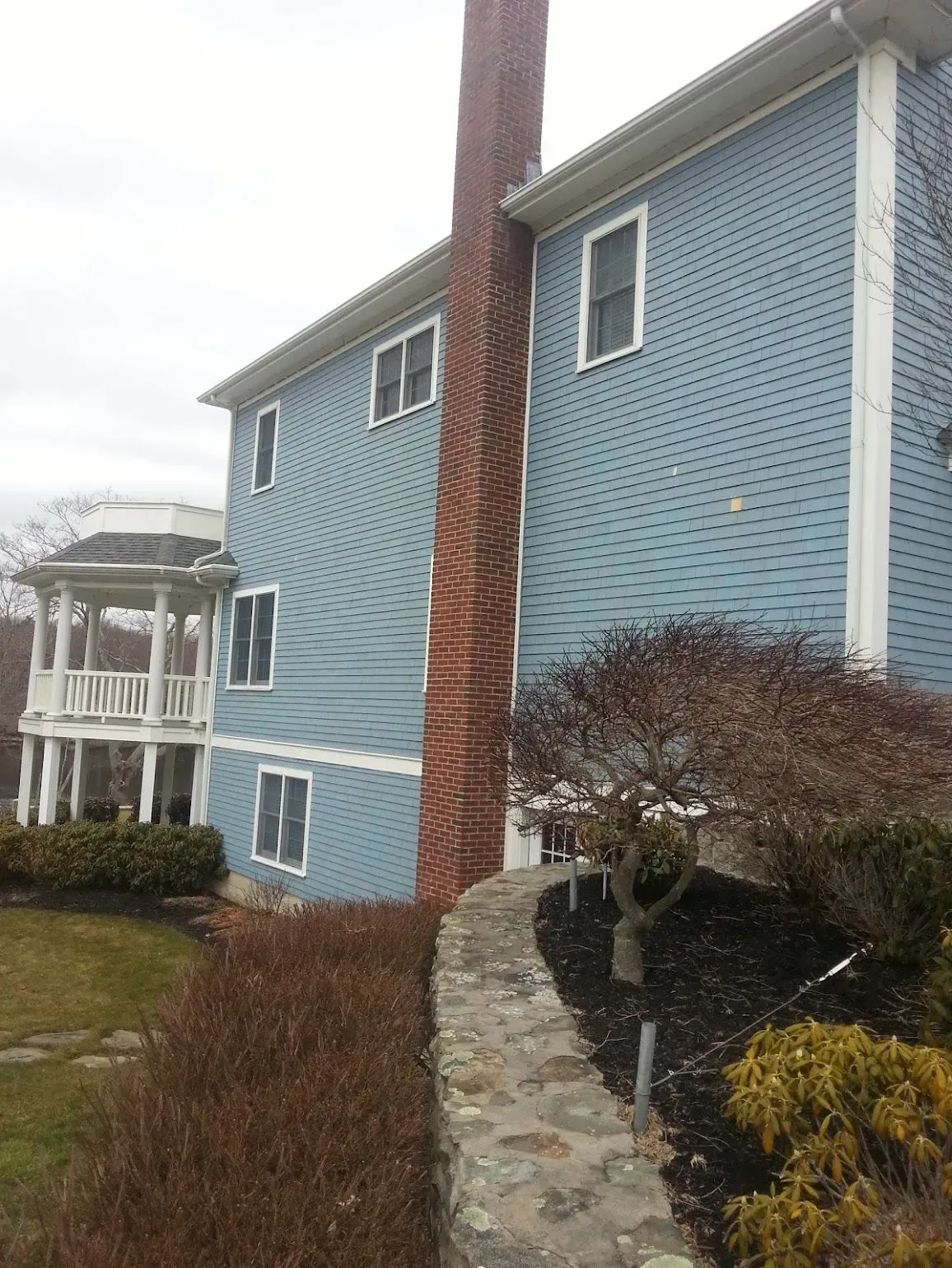 Blue house with a brick chimney, stone wall, and gazebo.