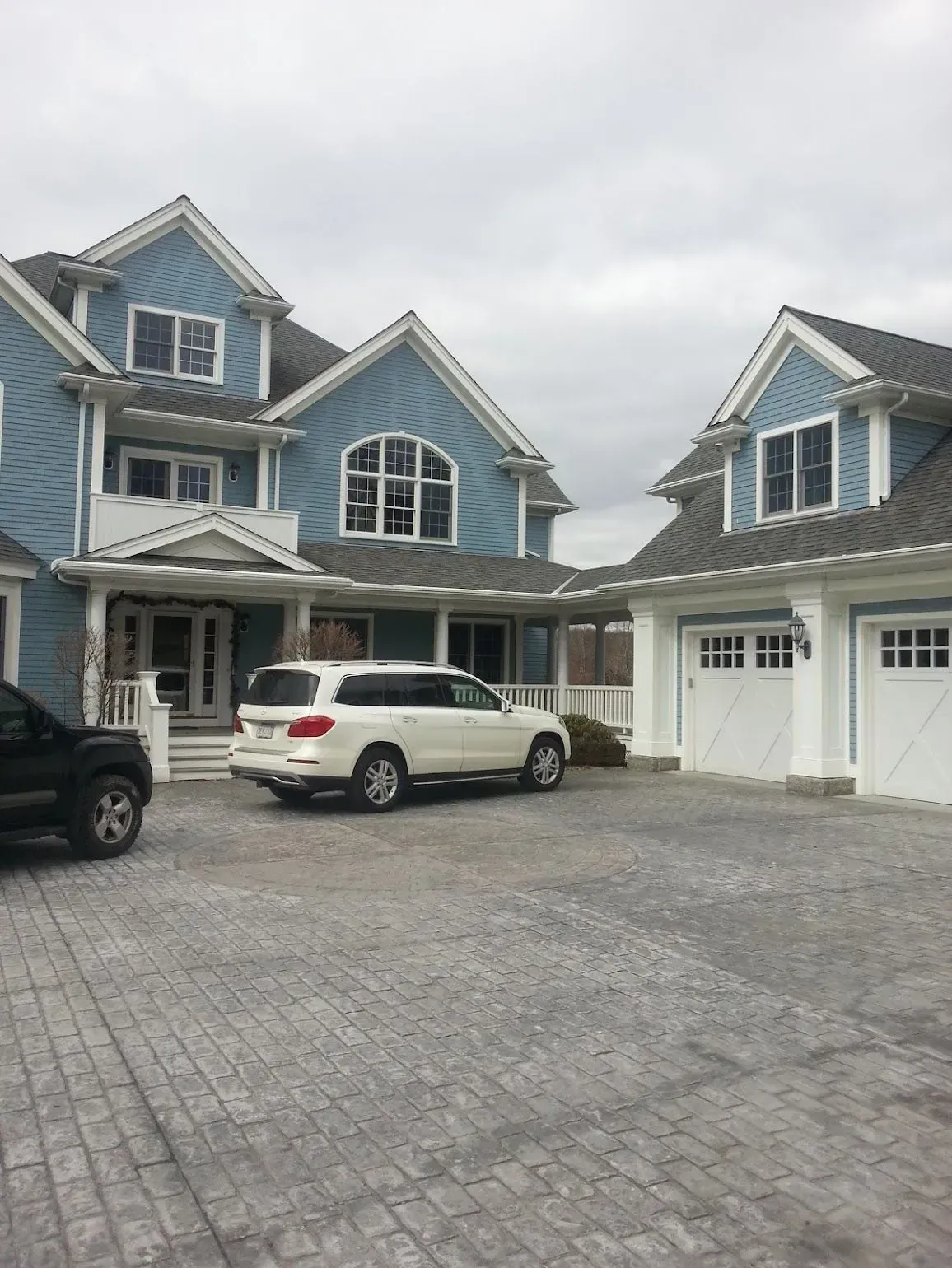 Blue house with white trim, attached garage, and a white SUV parked in the driveway. Overcast sky.