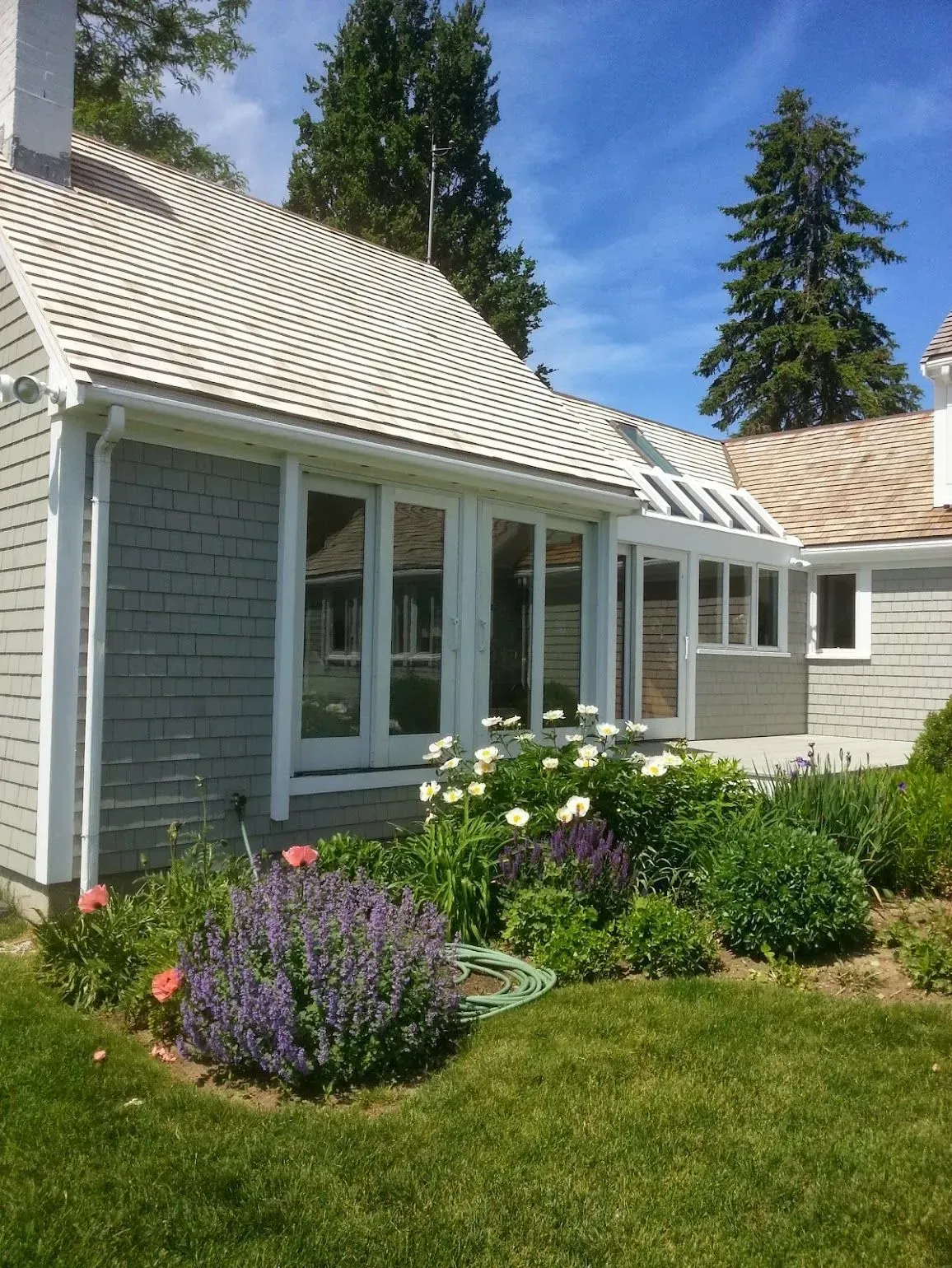 Gray shingled house with white trim, multiple windows, and a flower garden in front.