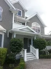 Gray house with white trim, ladders, and landscaping.
