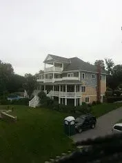 Large multi-story house with wrap-around balconies, green lawn, pool, and a portable toilet.