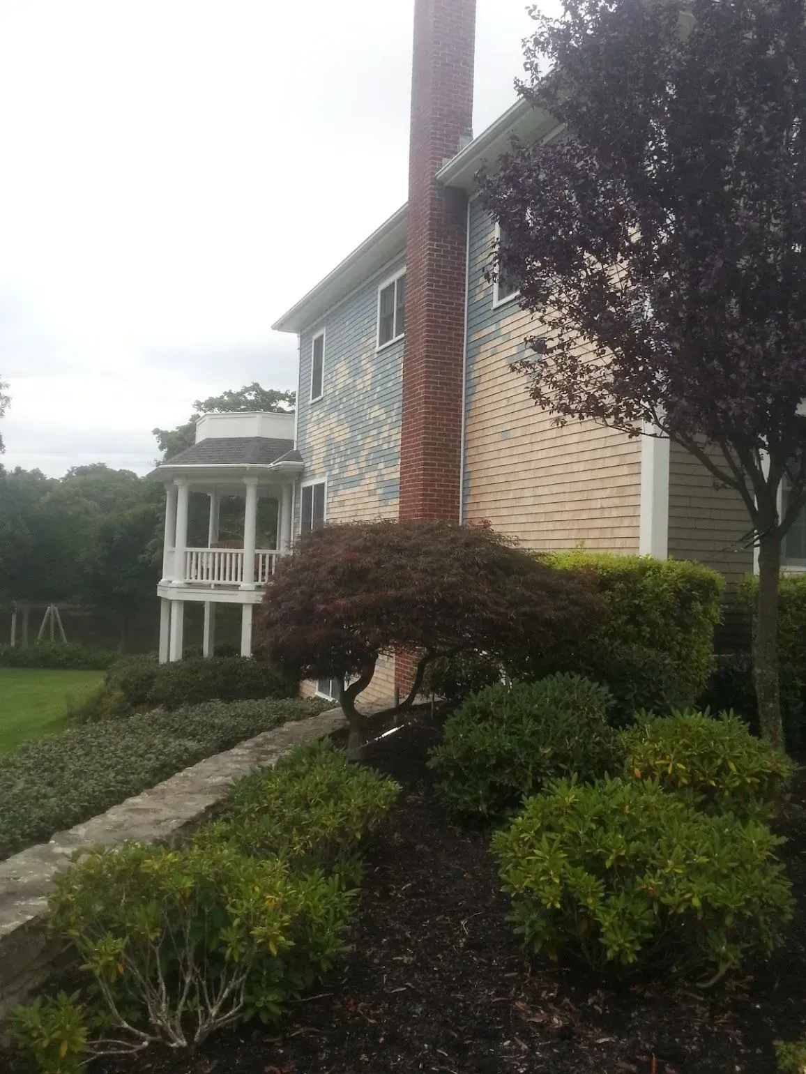 House with a chimney, porch, and landscaping. The house is light blue and tan, and the sky is overcast.