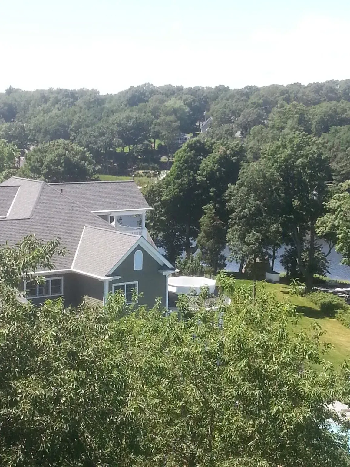 House with green siding and gray roof by a lake, surrounded by trees.