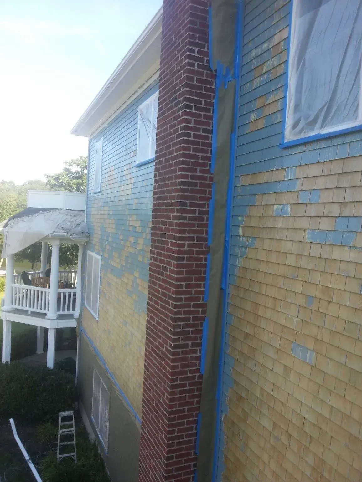 Side of house with brick chimney, weathered wooden shingles, and blue painter's tape.